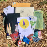 Photograph showing the ART & Justice Art Kits, containing pencils, sketchbooks, papers, bags, on a brown background